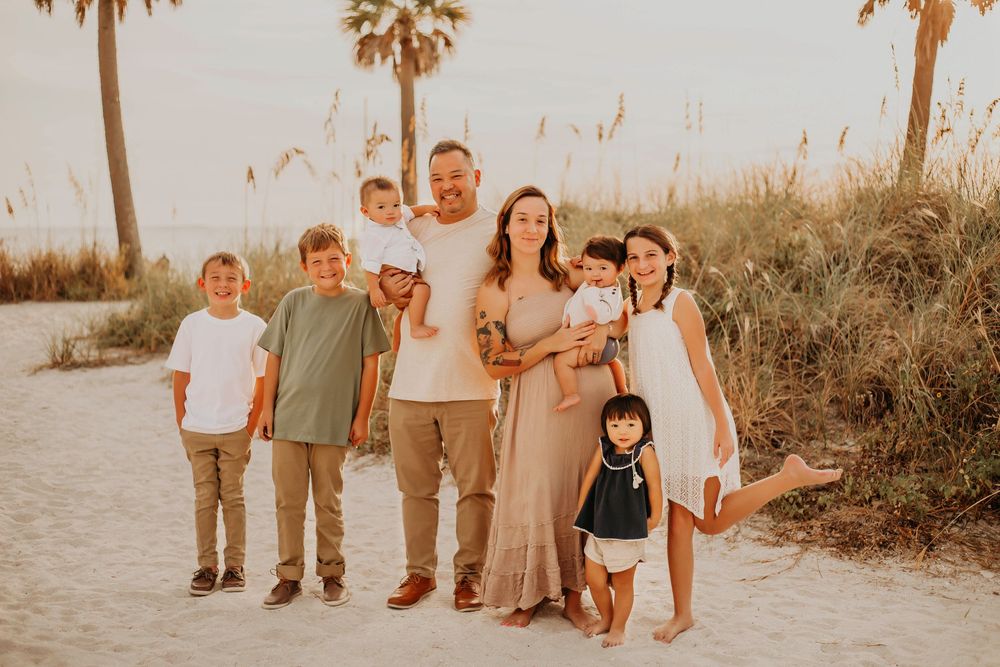 A family group poses together on a sandy beach path with palm trees and golden sunlight at sunset.