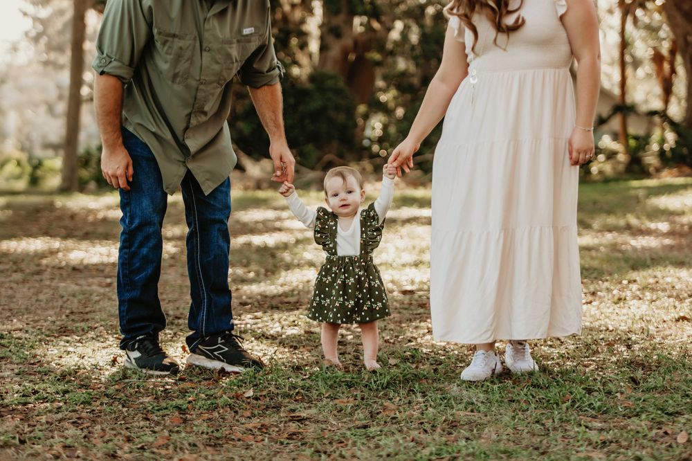 Family holds hands together in casual outdoor setting with white dress, denim and small floral dress.