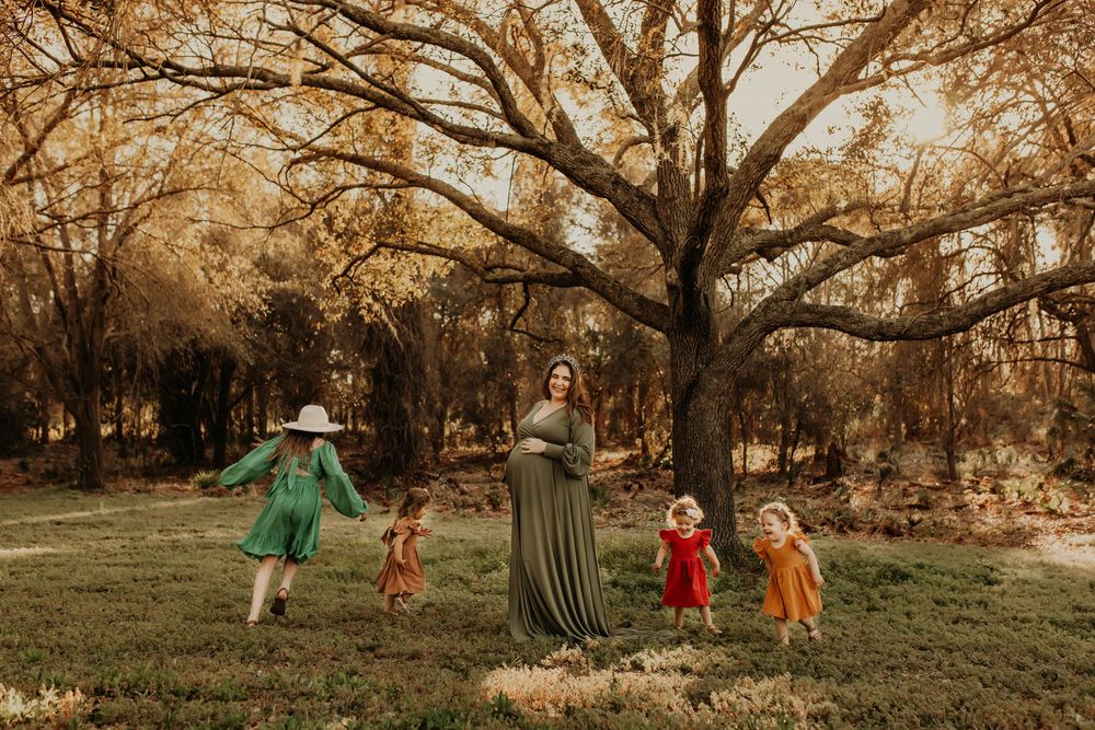 People in colorful dresses dance and play in a wooded autumn field with golden sunlight streaming through trees.