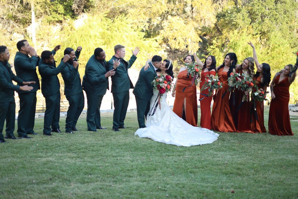 Wedding party stands in line on grassy lawn during outdoor autumn ceremony with trees in background.