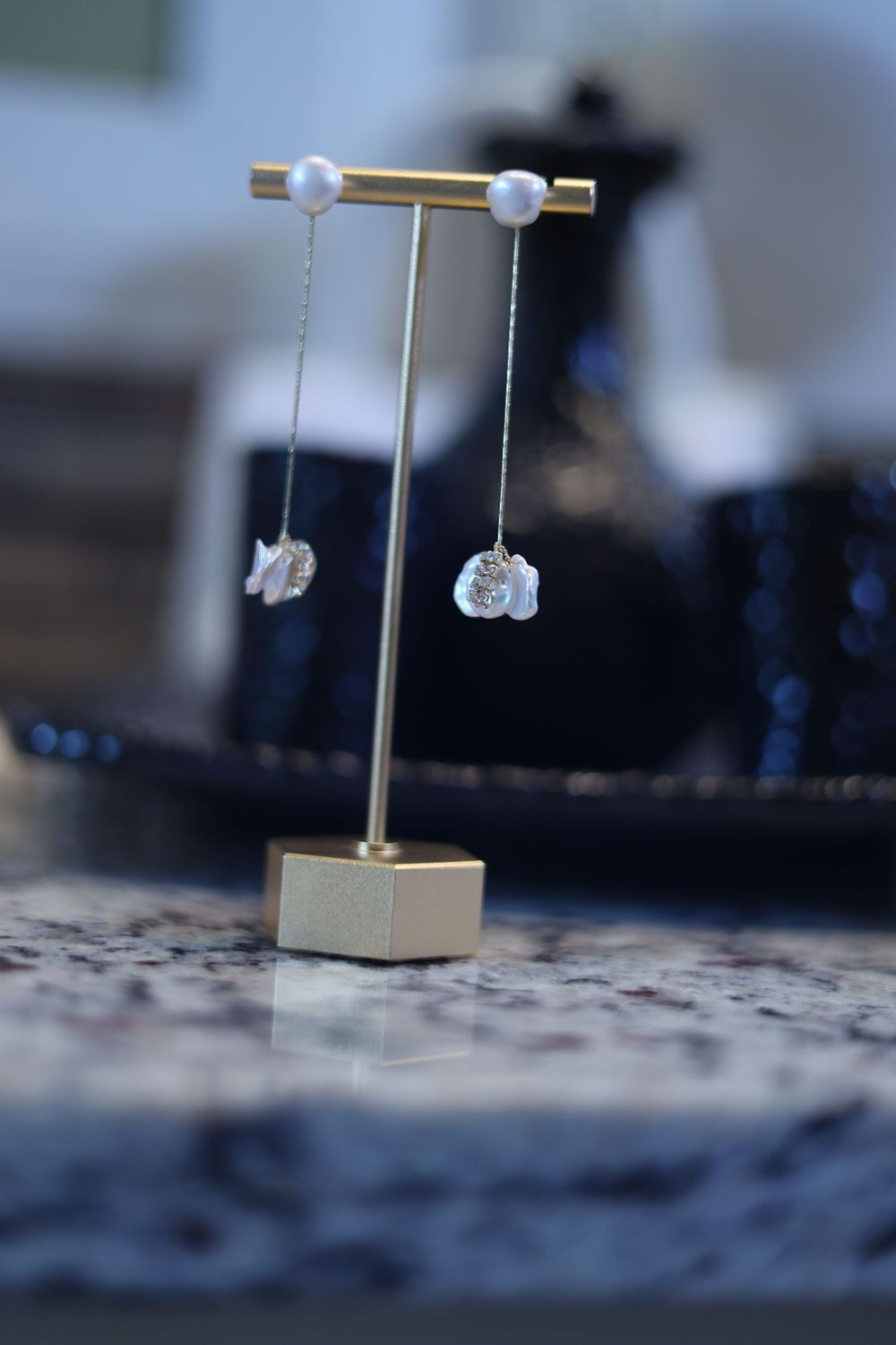 Pearl and gold earring stands displayed on a textured surface with soft focus background.