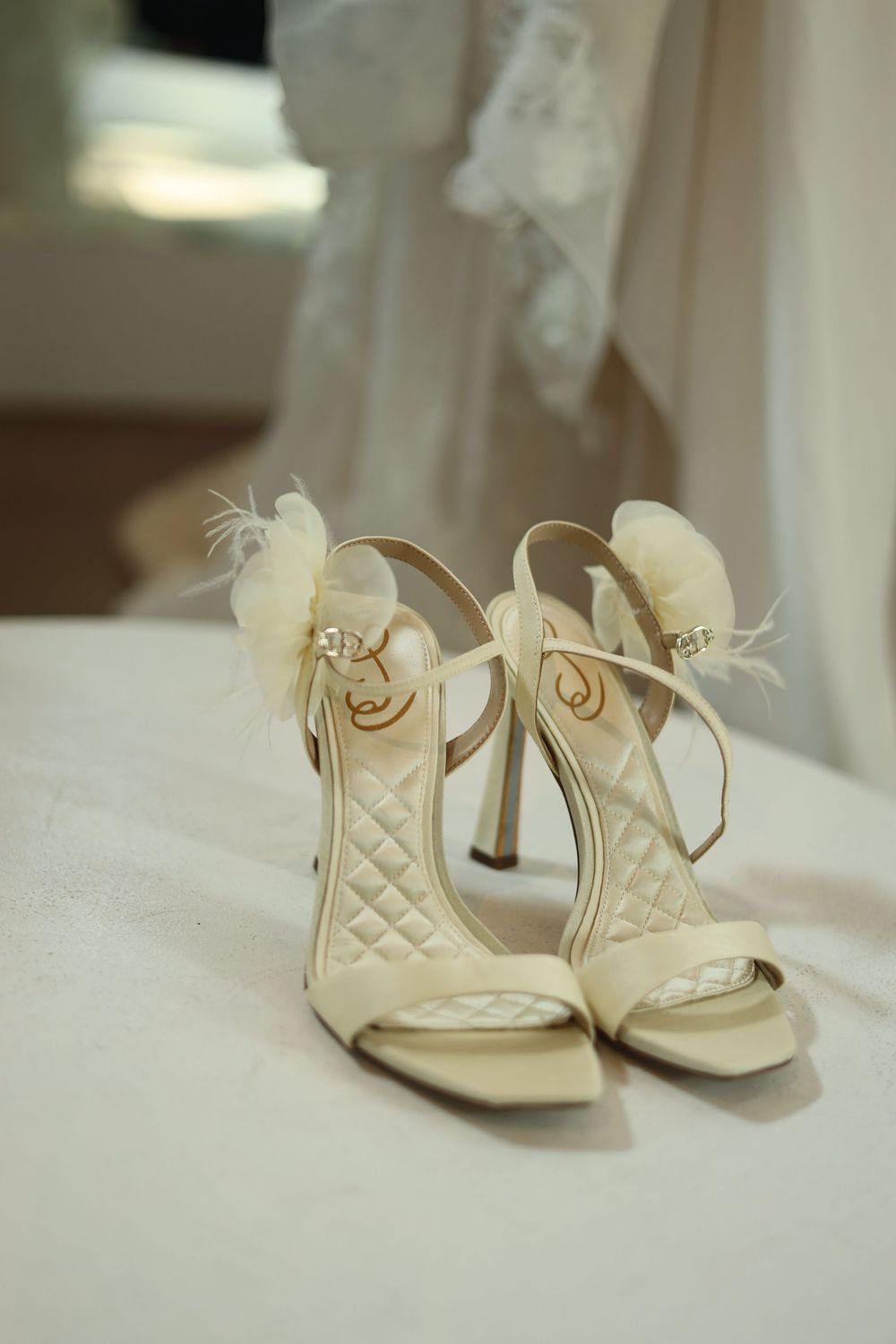 A series of elegant cream-colored quilted bridal shoes with delicate straps and feather details shown from different angles.
