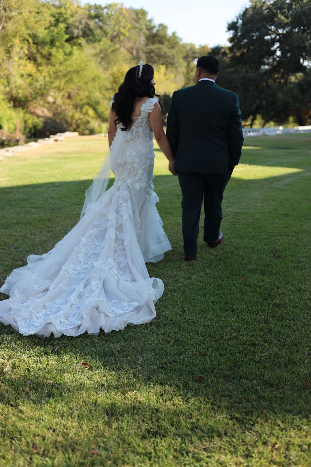 Wedding dress train flowing behind couple walking on green grass during outdoor ceremony.