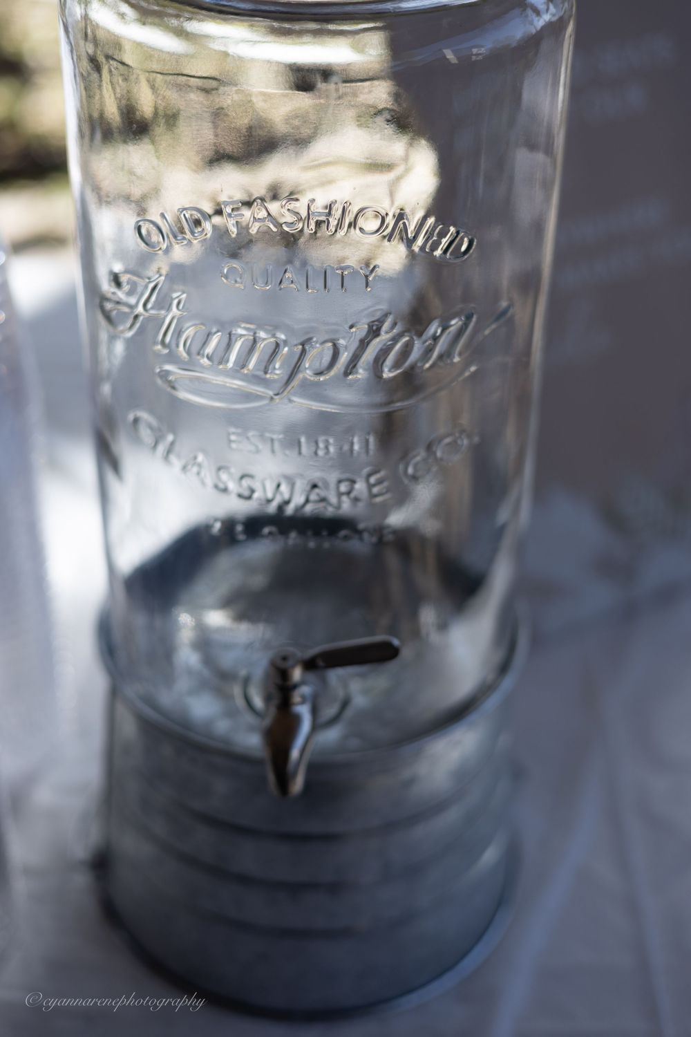 Close up detail of vintage Hampton glass beverage dispenser with metal spigot showing embossed lettering.