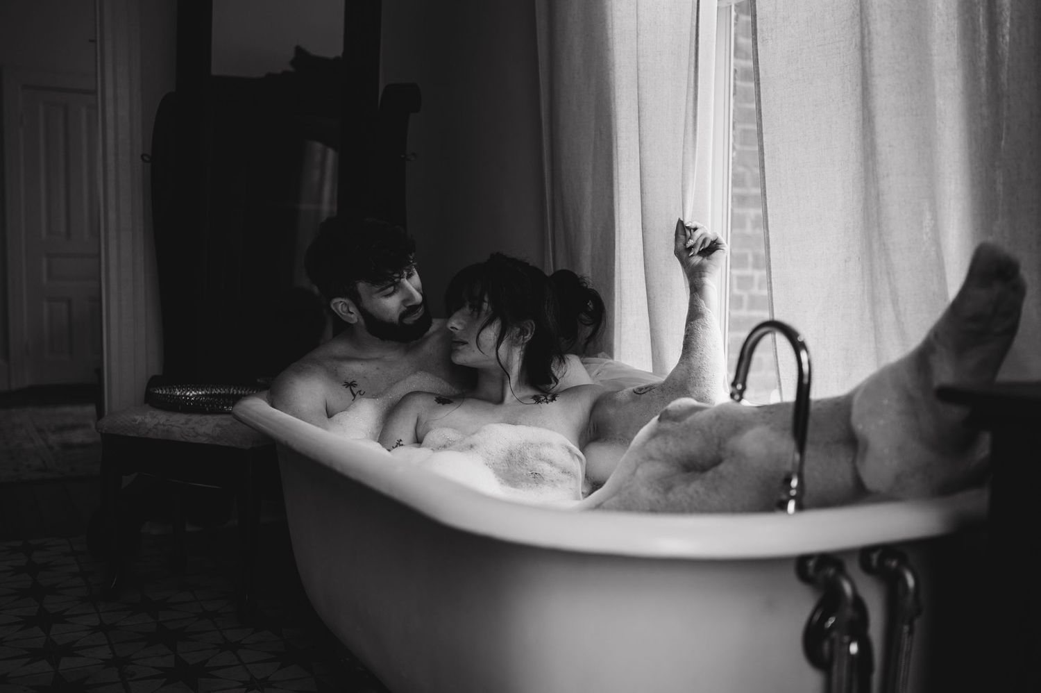 A dog peers over the edge of a vintage clawfoot bathtub in this black and white photograph.