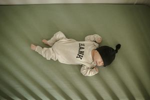 Newborn in white onesie sleeping on green textured surface.