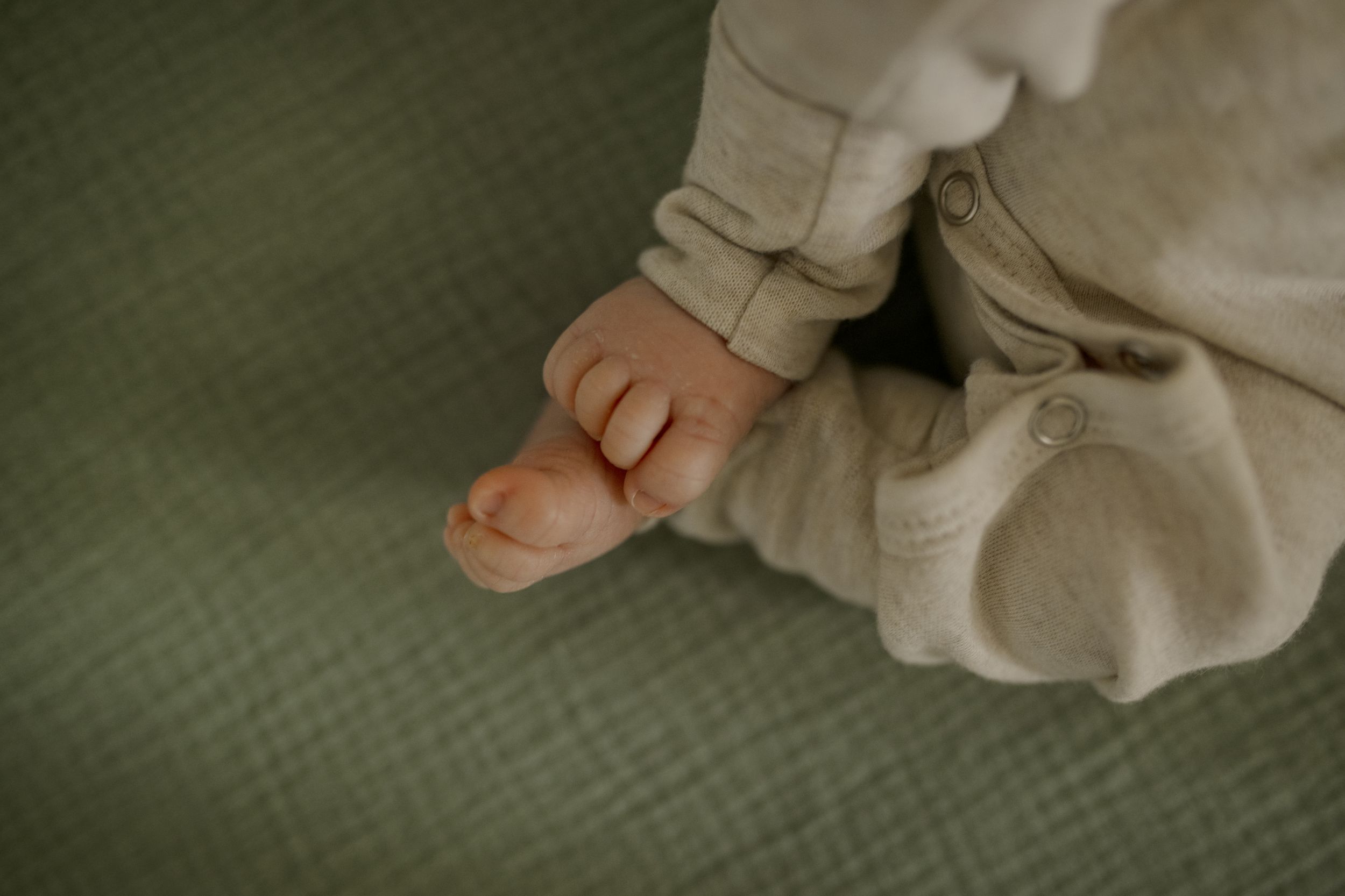 Close-up of tiny baby feet in white clothing on green textured fabric.