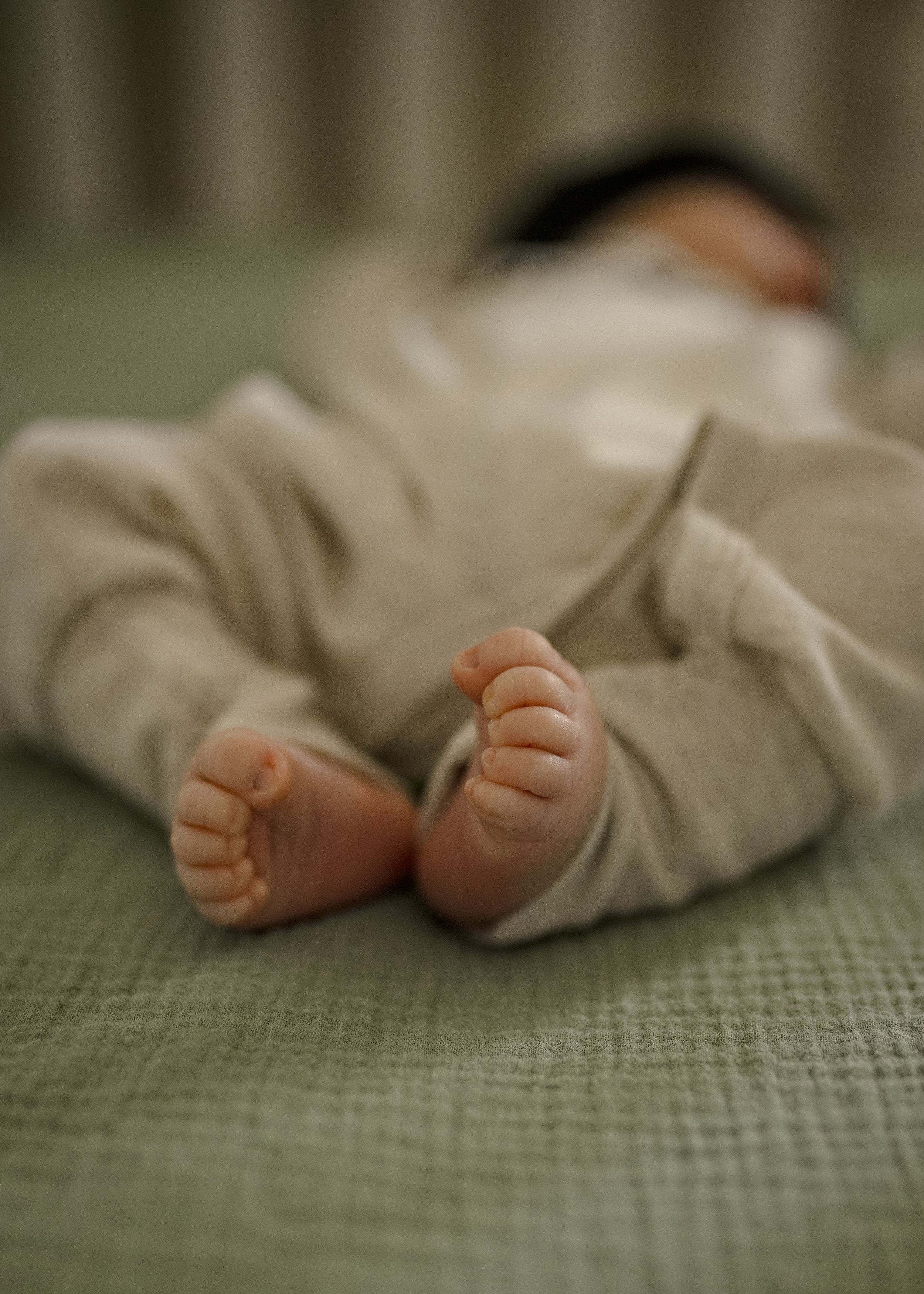 Small bare feet of sleeping baby wearing cream-colored outfit on textured green surface.