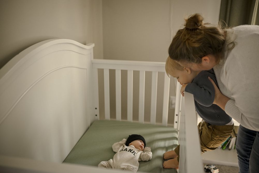 White wooden crib with mint green mattress in nursery corner setting.