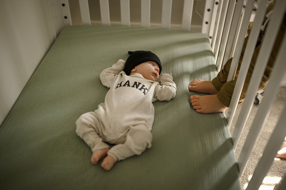 A baby wearing a Giants onesie lies on a green couch cushion.