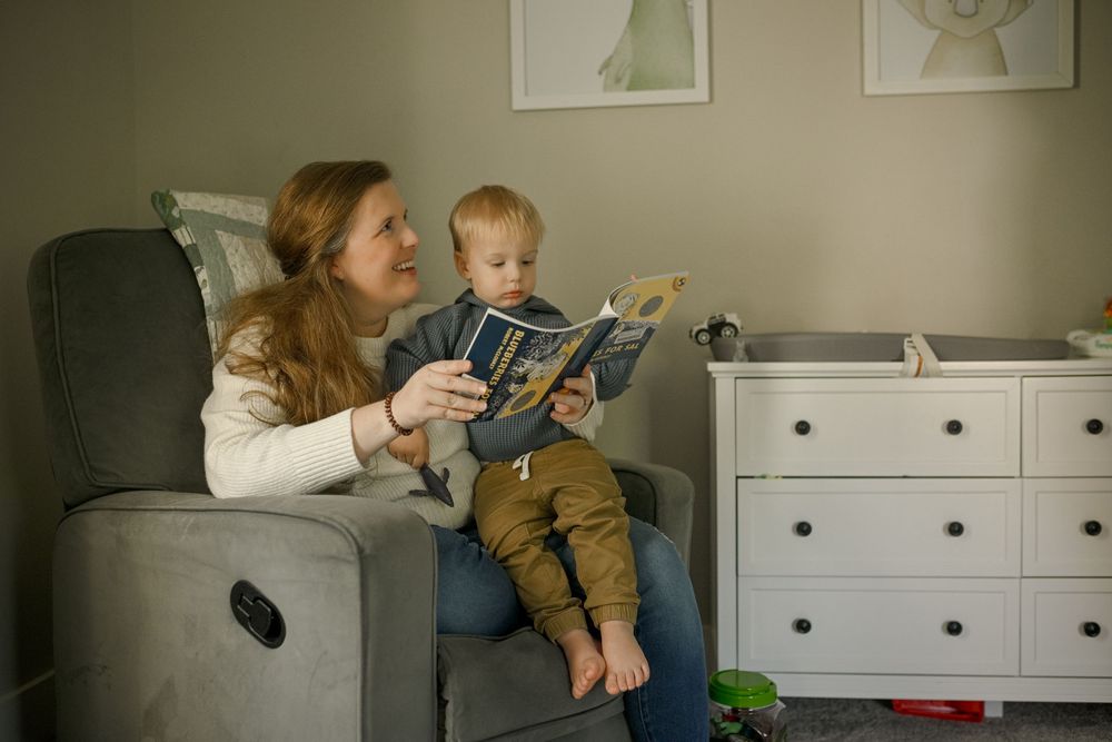 A cozy reading session on a white bed with toys and books.