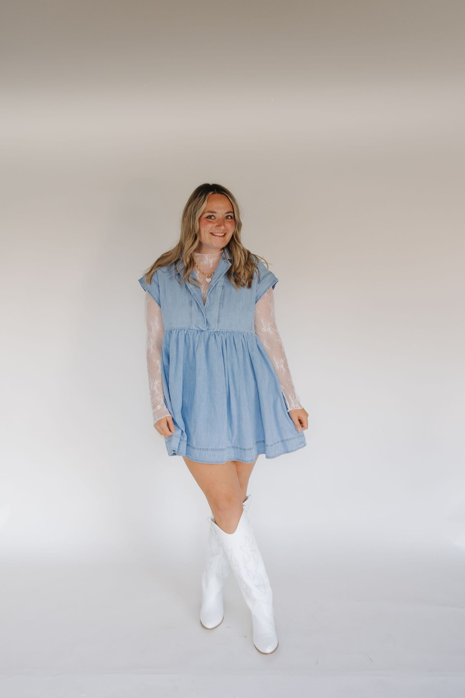 A woman in a light blue babydoll dress and white cowboy boots poses against a neutral background.