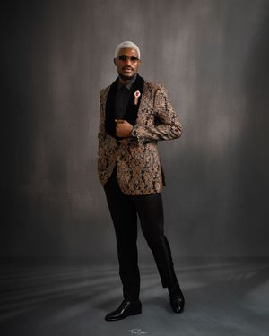 A person models a stylish brown patterned blazer with black pants and dress shoes against a dark gray studio backdrop.