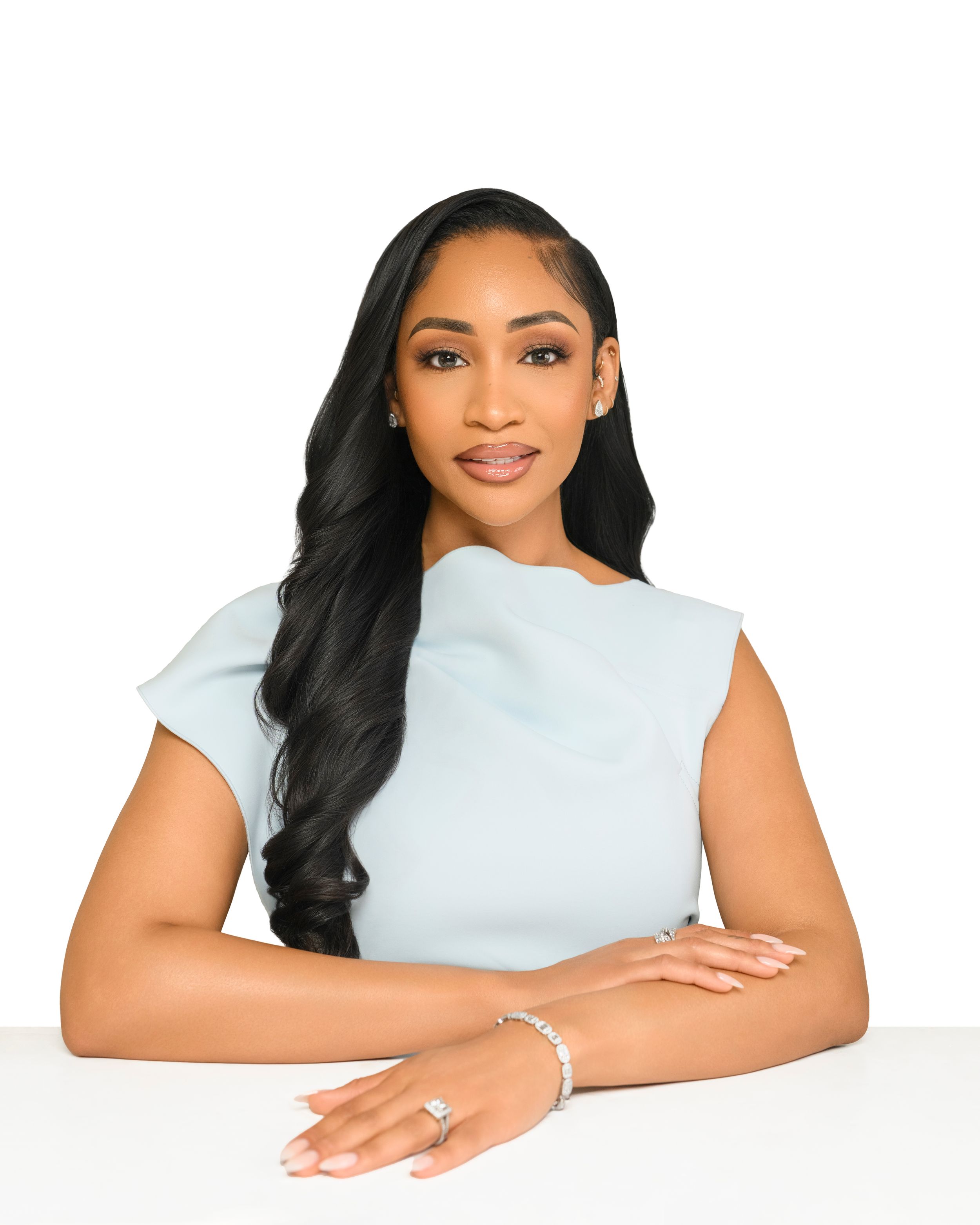 A person in a light colored top poses with long dark hair against a white background in a professional headshot series.