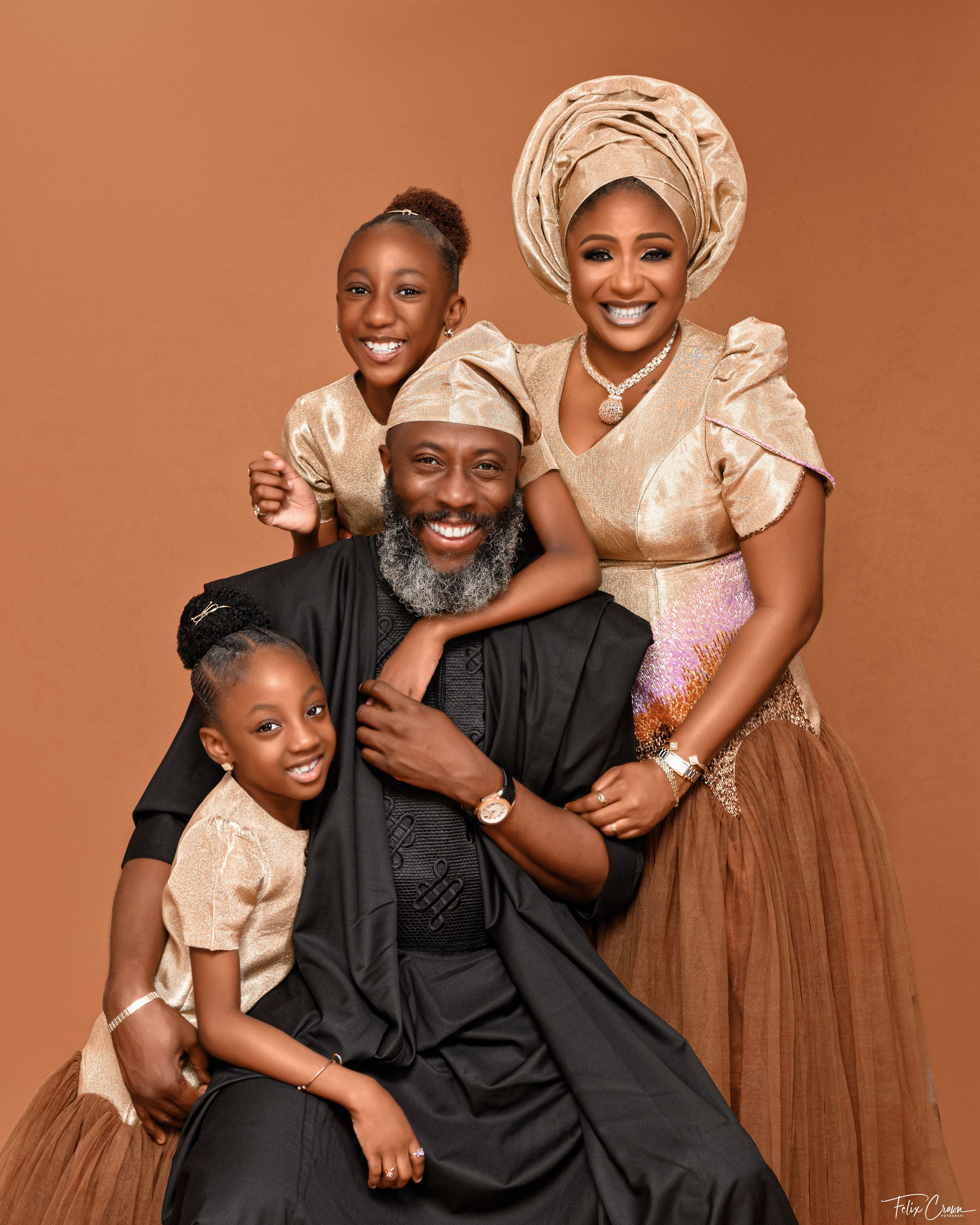 Traditional African family portrait on warm brown background with matching cream and gold outfits.