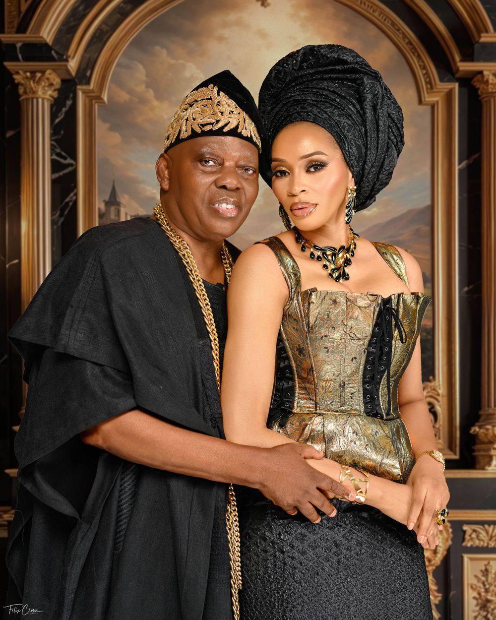Traditional Nigerian formal portrait featuring couple in black and gold attire against architectural background.
