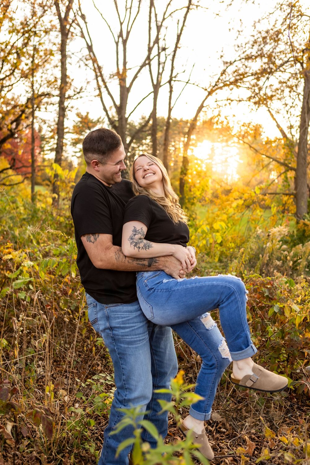 A couple shares an intimate moment at sunset in a golden autumn field with tall grass and trees.