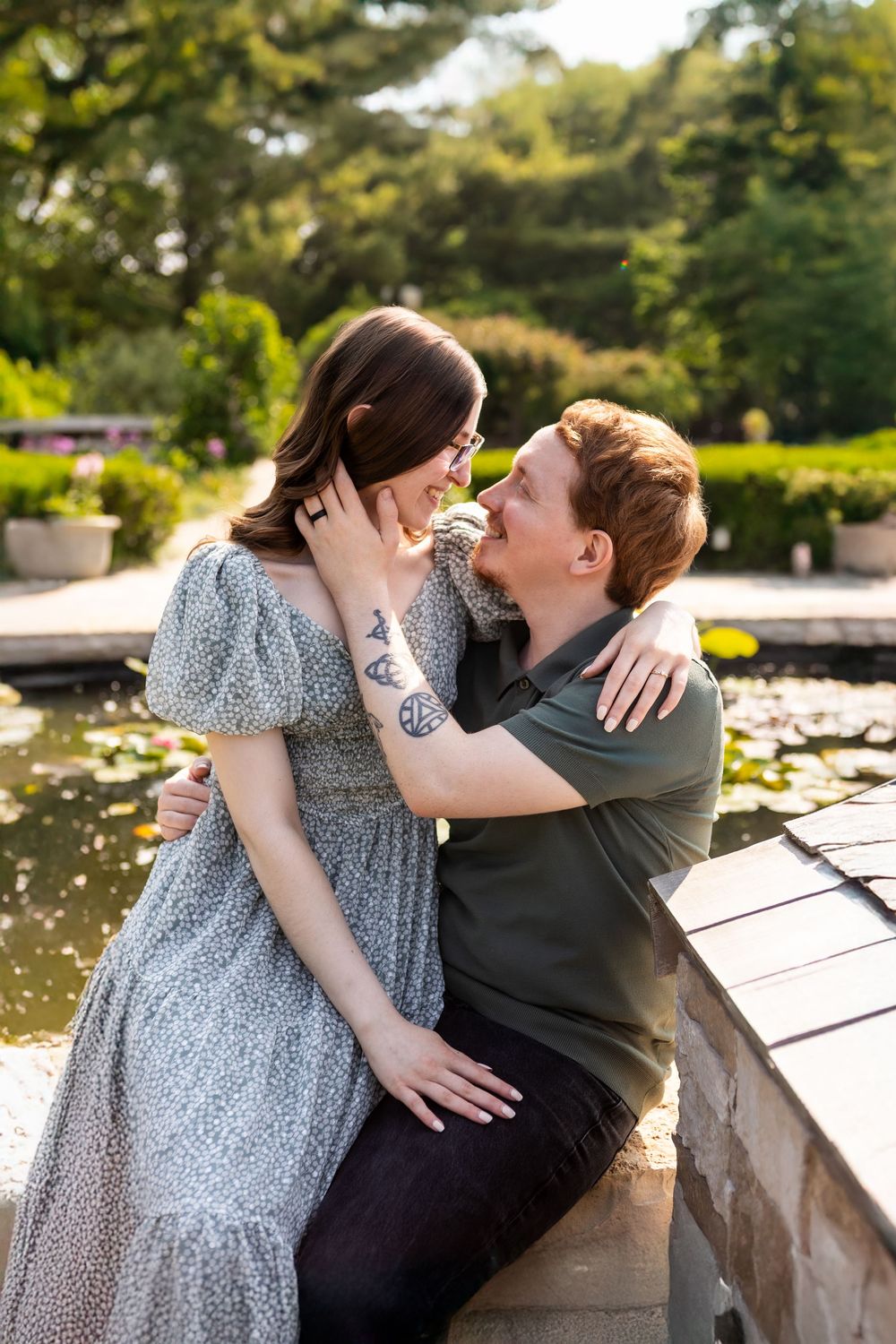 A romantic couple embraces by a garden pond on a sunny afternoon, sharing an intimate moment in nature.