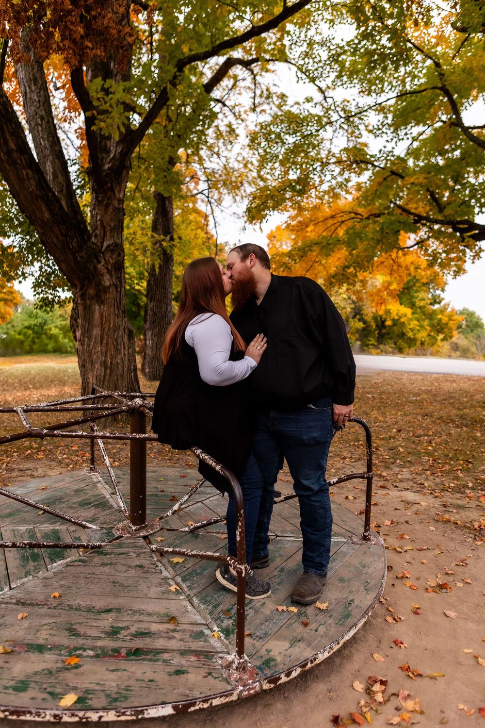 A couple shares a romantic moment on a rustic wooden bridge surrounded by autumn foliage and fallen leaves.