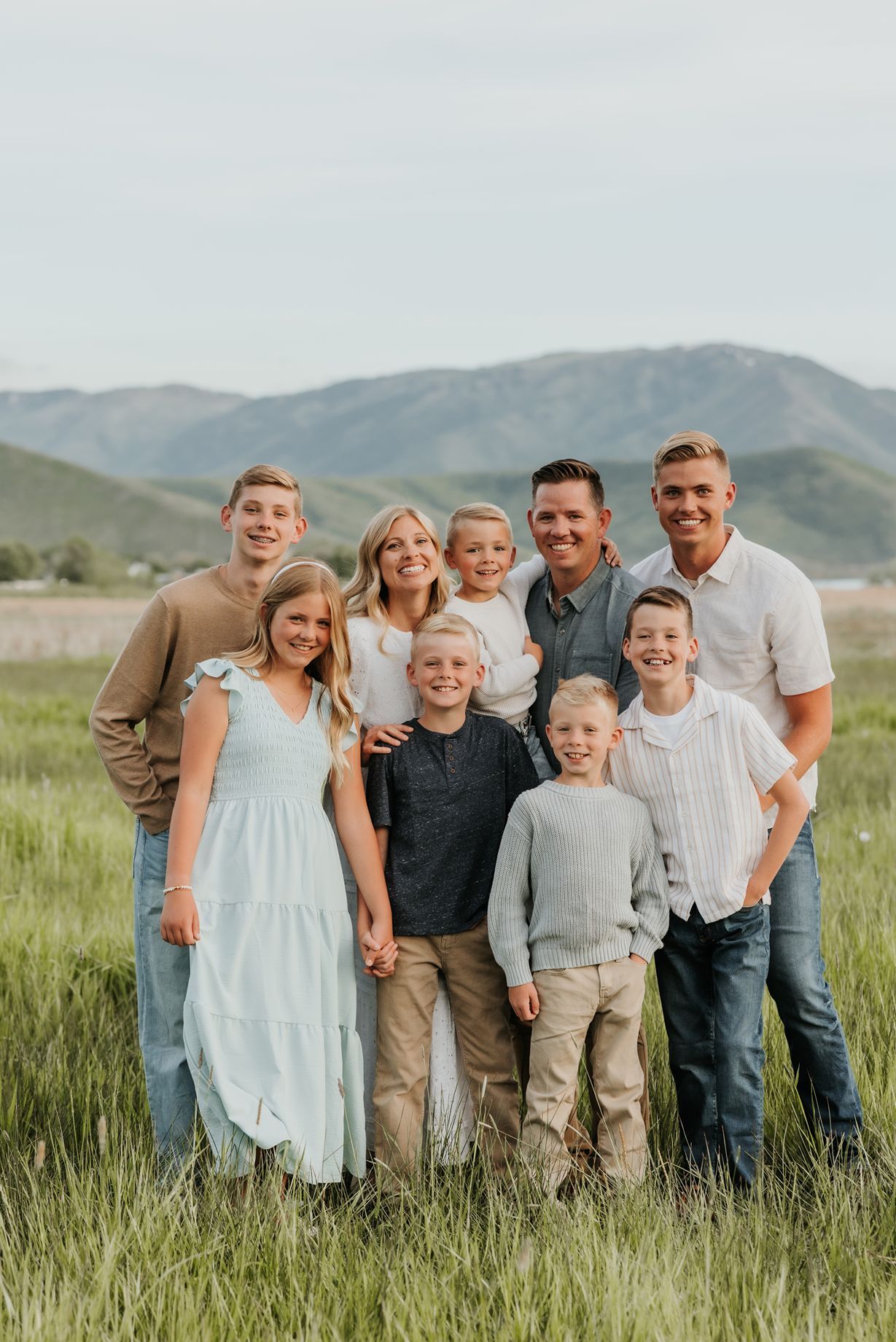 Extended family group portrait in casual attire standing together in green mountain meadow.