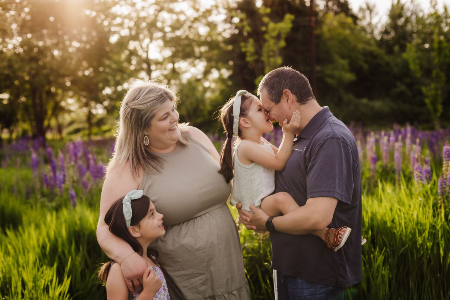 A family shares a tender moment in a field of purple lupine flowers at sunset.
