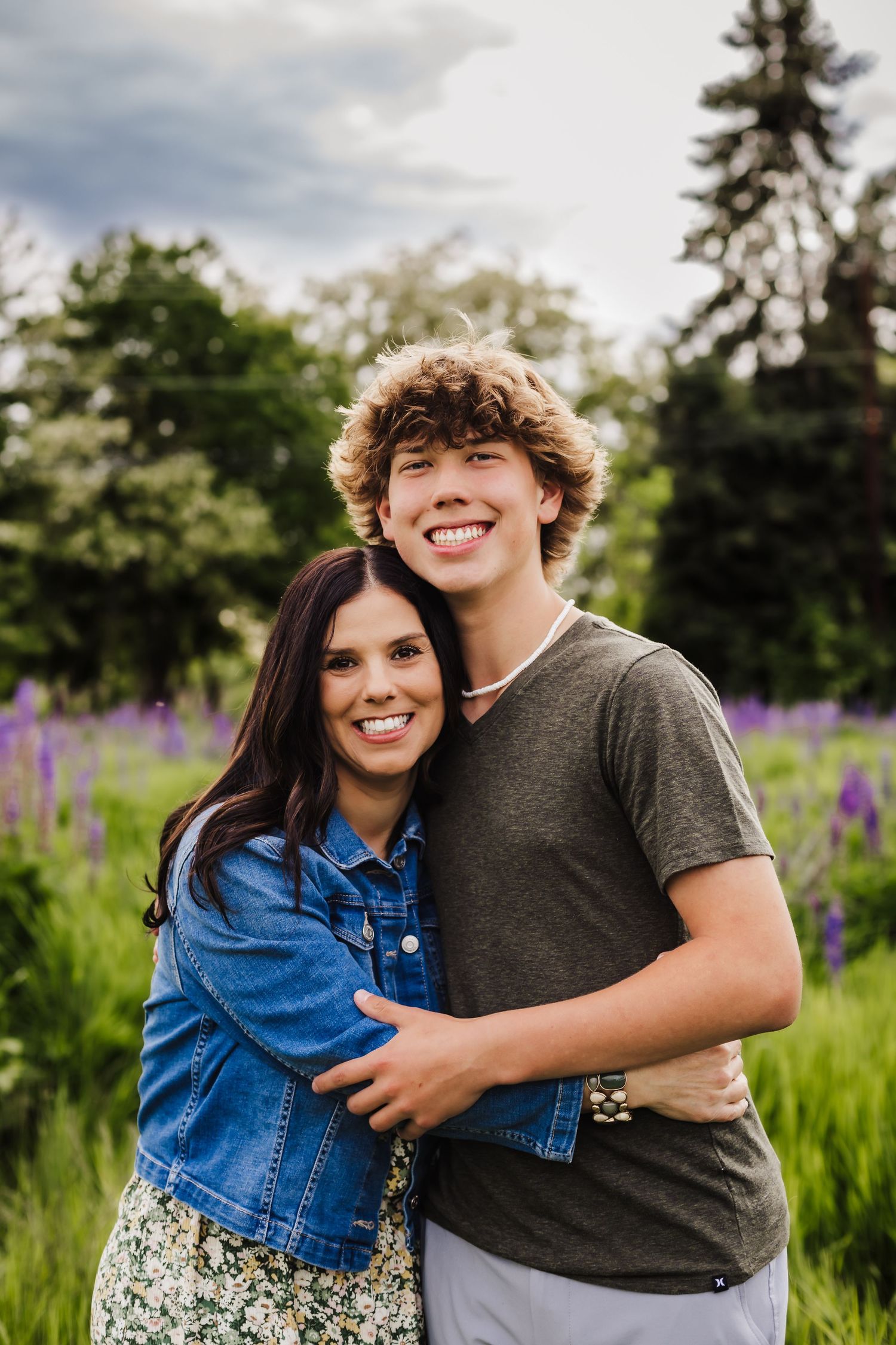 A couple poses together in a field of purple lupine flowers during golden hour.