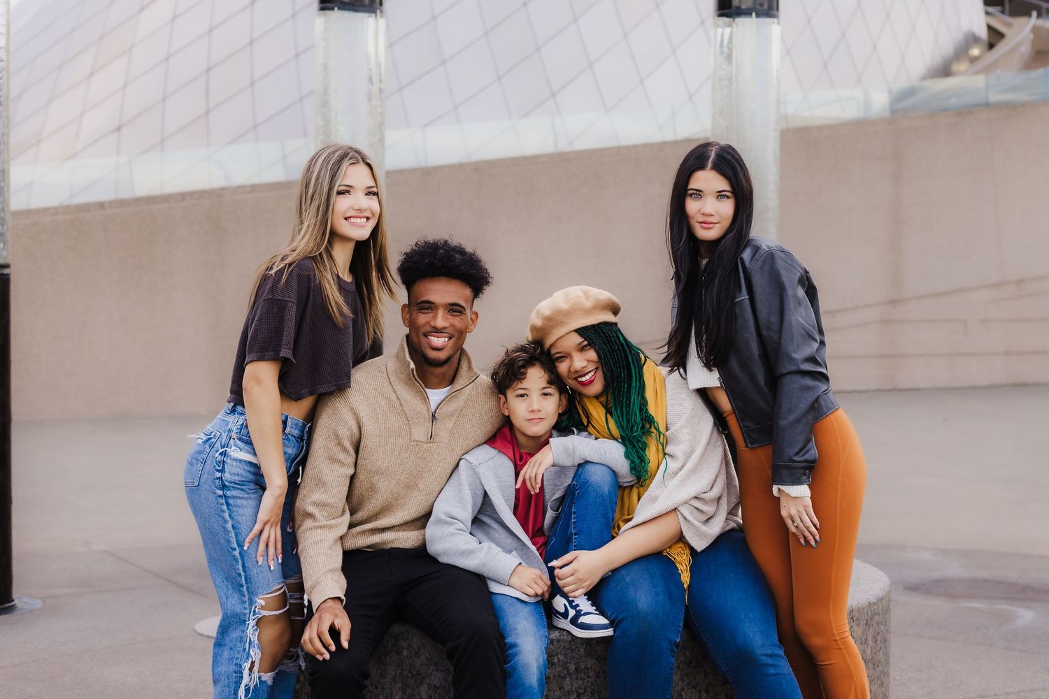 A diverse group of friends sitting together and smiling against a white wall.