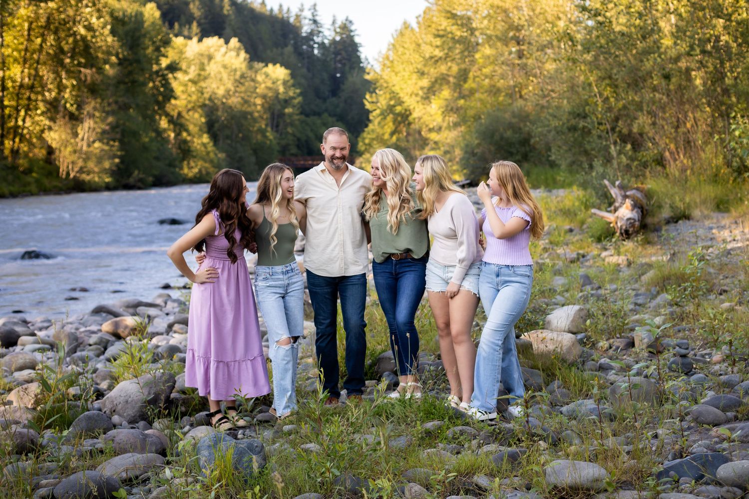 A group enjoying a sunny day by the riverside with trees and rocks in the background.