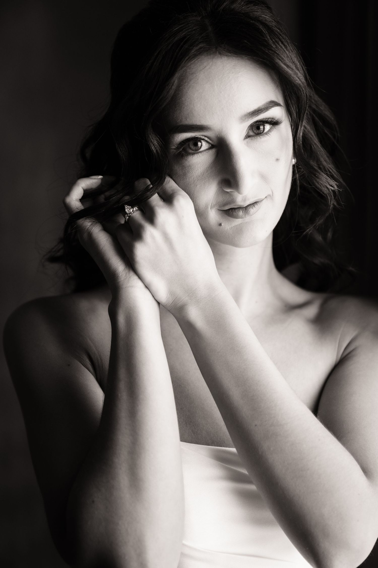 A black and white portrait in dramatic lighting shows a woman in a sleeveless top with curled dark hair and gentle expression.