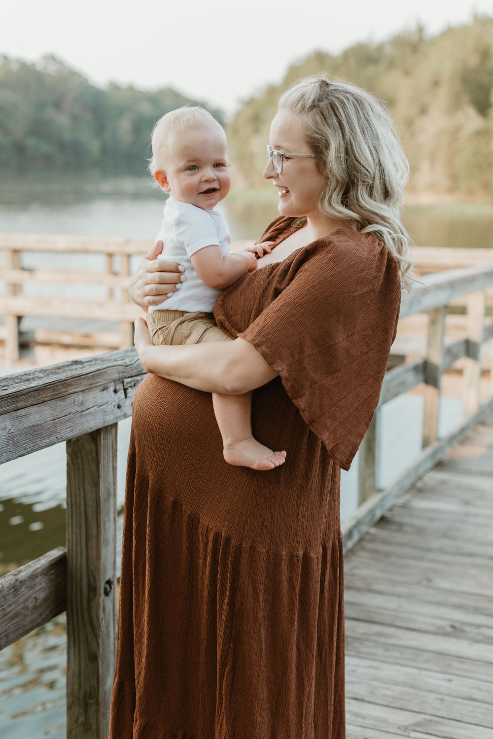 Mother and baby sharing tender moments on wooden dock during golden hour.