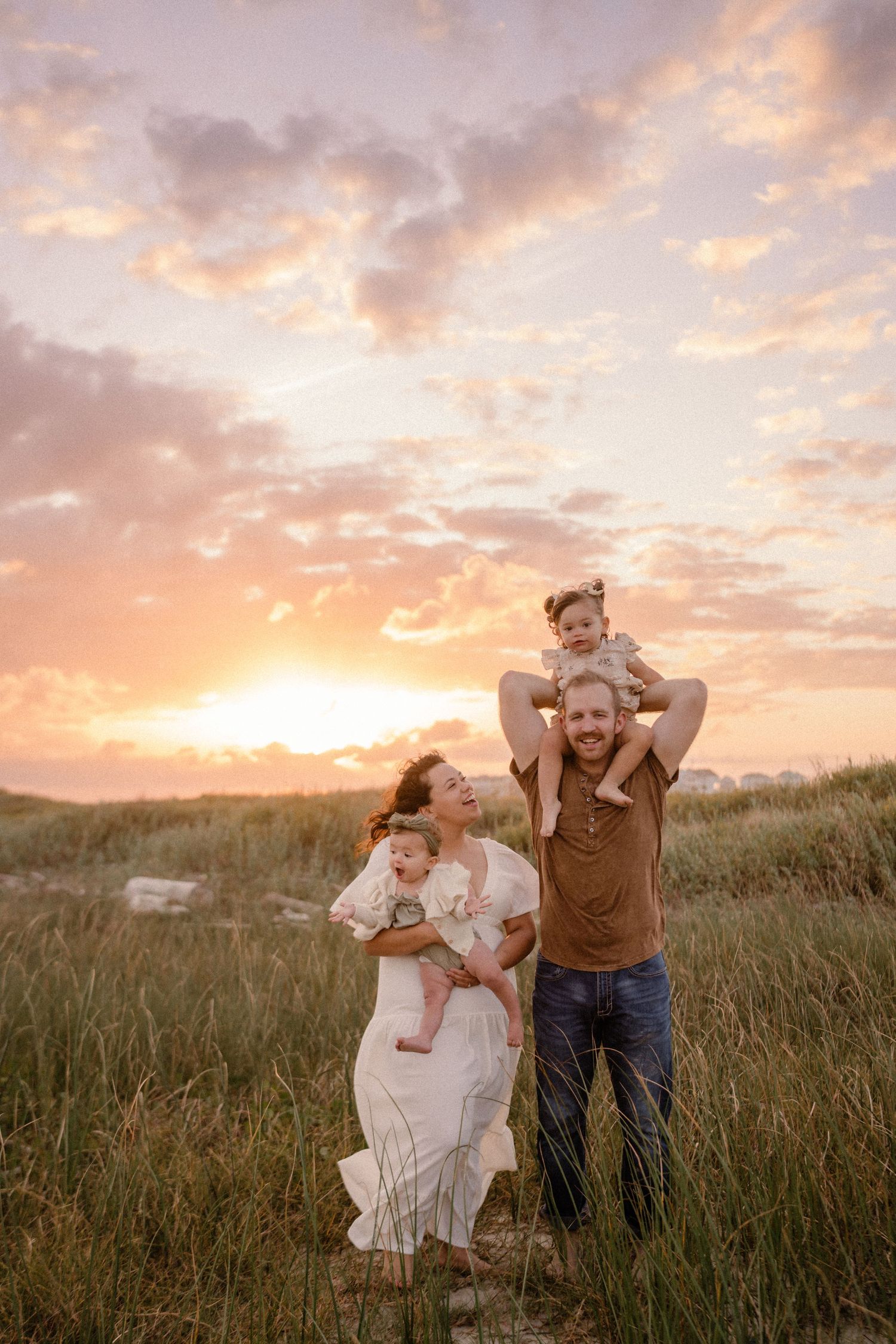 Family enjoying a beautiful sunset together in a grassy meadow with dramatic pink and orange clouds in the sky.