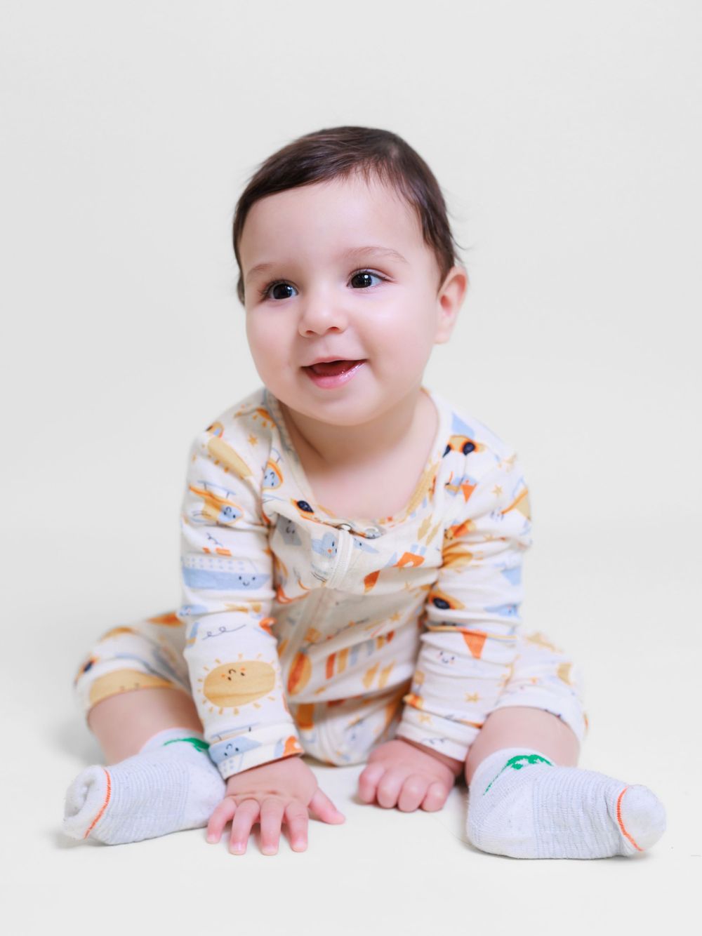 Smiling baby in a patterned onesie sitting on a neutral background. Toronto family photography.
