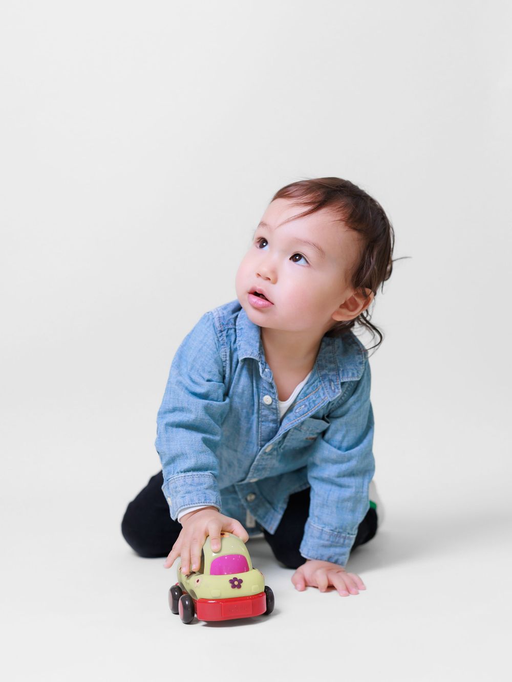 Toddler in a denim shirt and black pants playing with a toy car on a neutral background. Toronto family photography.