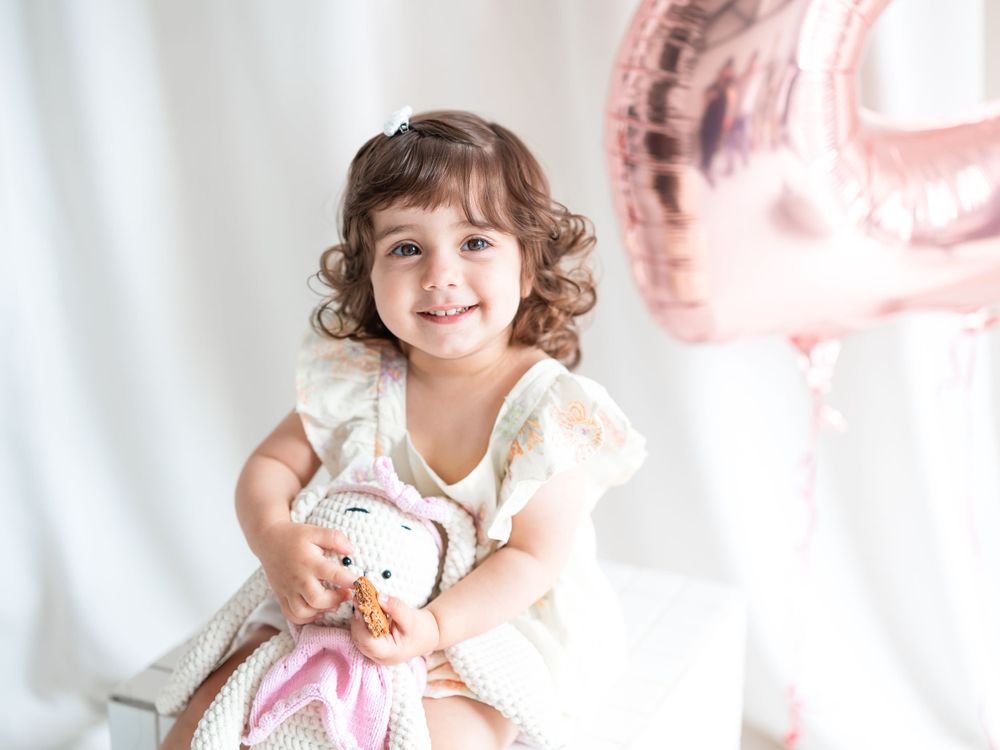 Smiling young girl holding a stuffed toy with a pink birthday balloon in the background. Toronto family photography.
