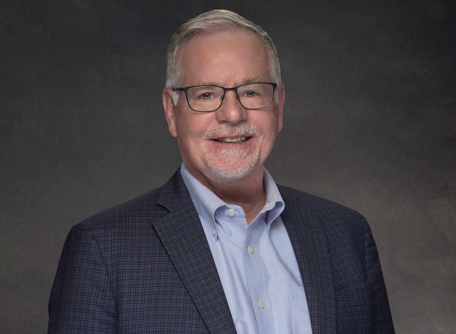 Gray-haired man in dark checked sport coat smiling in headshot portrait