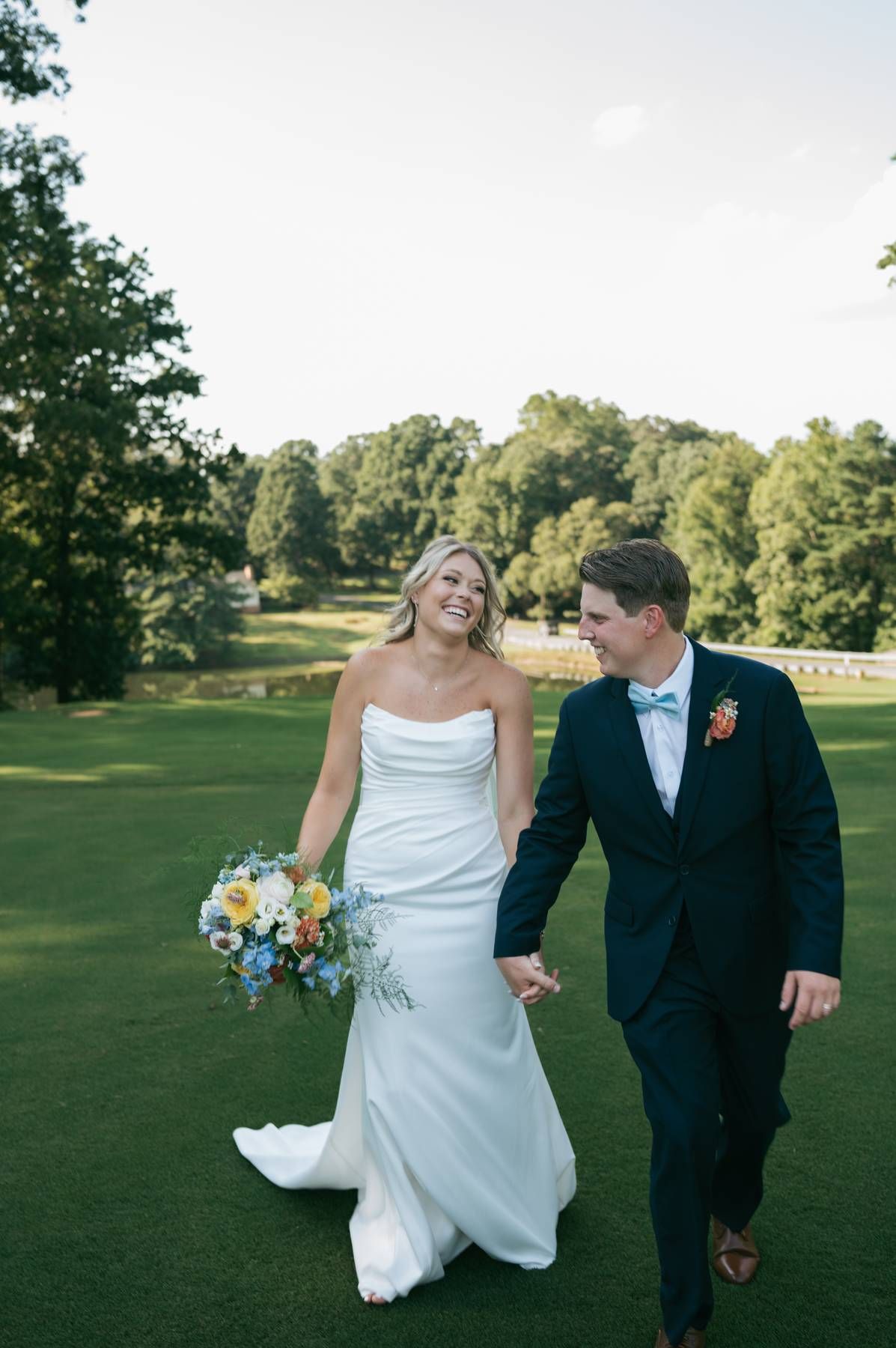 Happy bride and groom walking hand in hand on golf course in wedding attire Greensboro NC