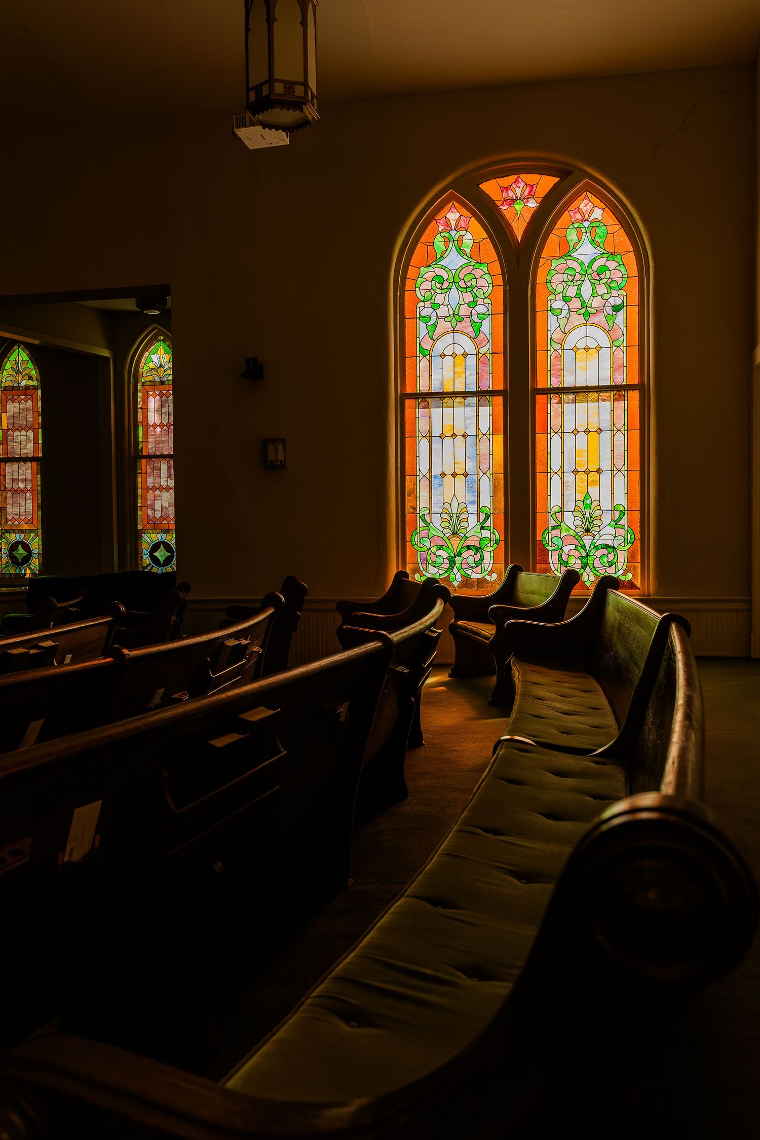 Beautiful stained glass windows illuminate a traditional church sanctuary with wooden pews.