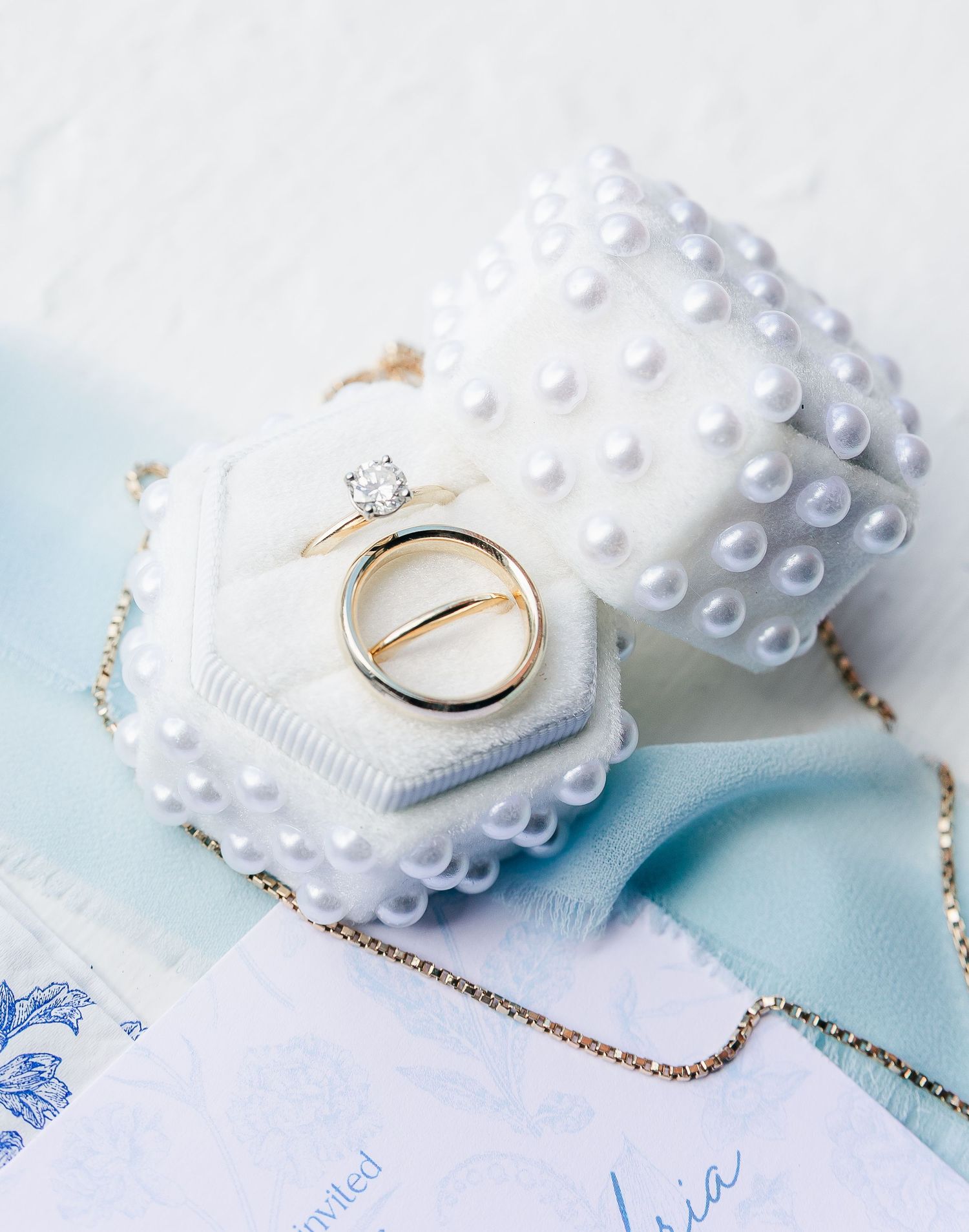 Wedding rings and delicate pearl details arranged on light blue and white stationery.