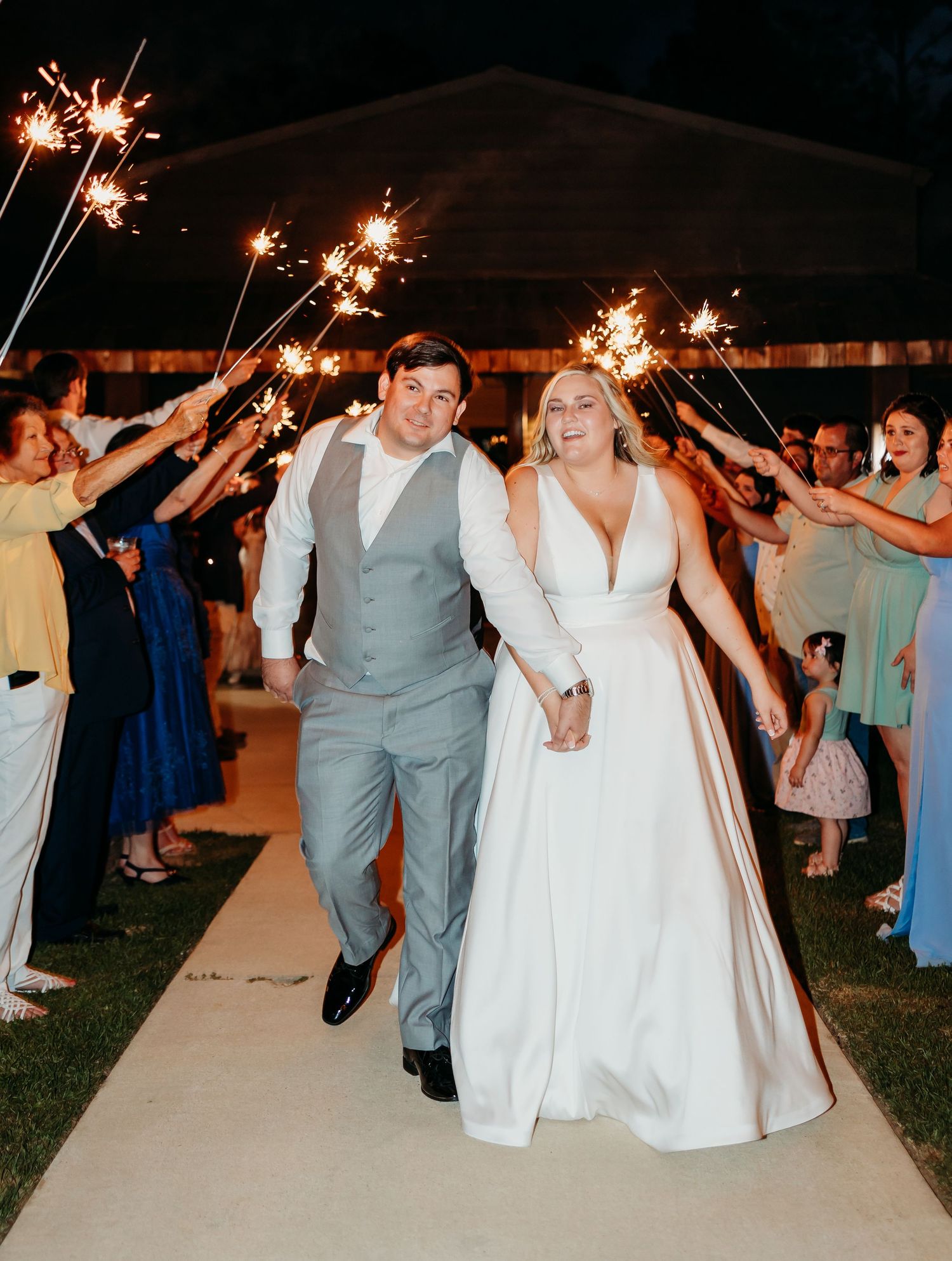 Wedding guests line a walkway holding sparklers as the newlyweds make their grand exit during an evening celebration.