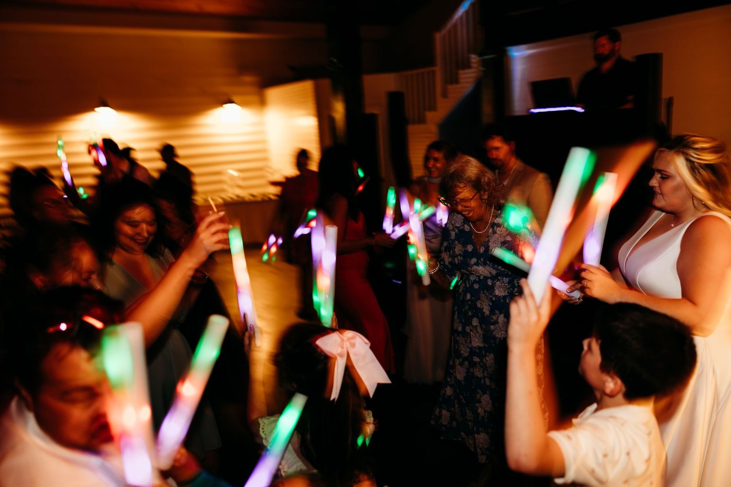 People dancing and celebrating at a party with glowing green light sticks creating a festive atmosphere.