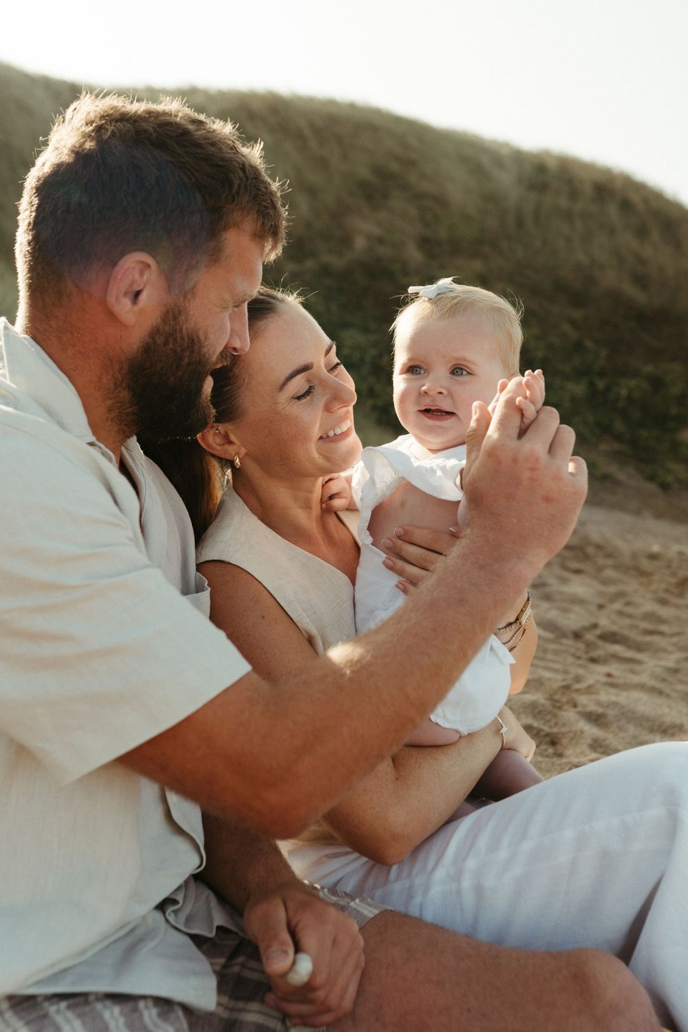 Young family sharing a tender moment together outdoors at sunset on a beach during a photo session.