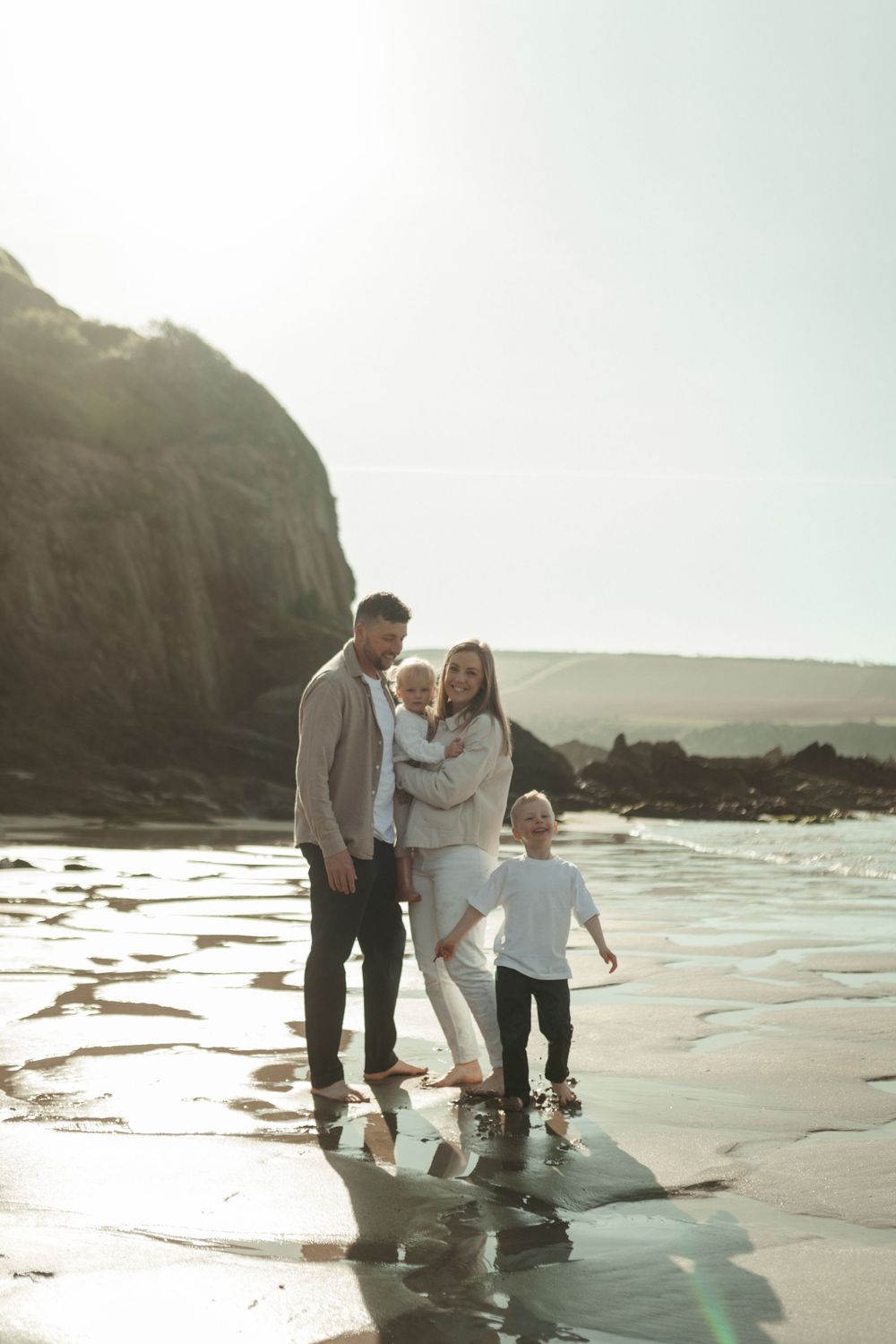 Family enjoying a sunset beach walk together along the shoreline with cliffs and ocean waves in the background.
