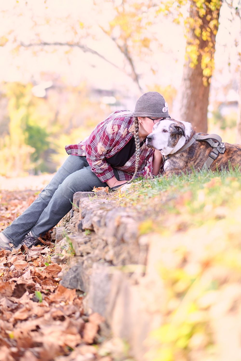 A person lying in fallen autumn leaves while wearing a plaid shirt and jeans on a sunny fall day.