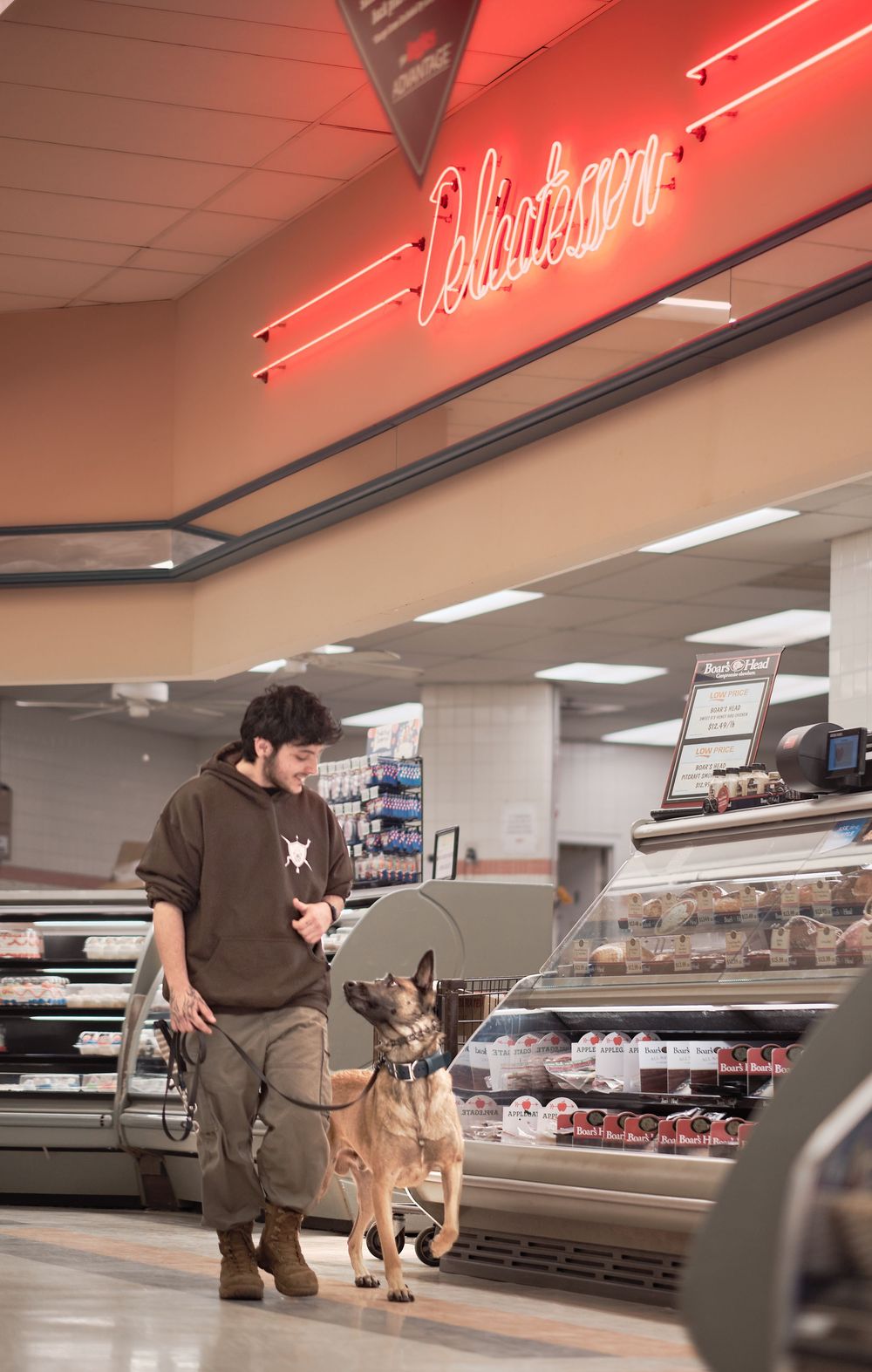 A police K9 unit performs a narcotics search near a red-lit refrigeration case in a retail store.