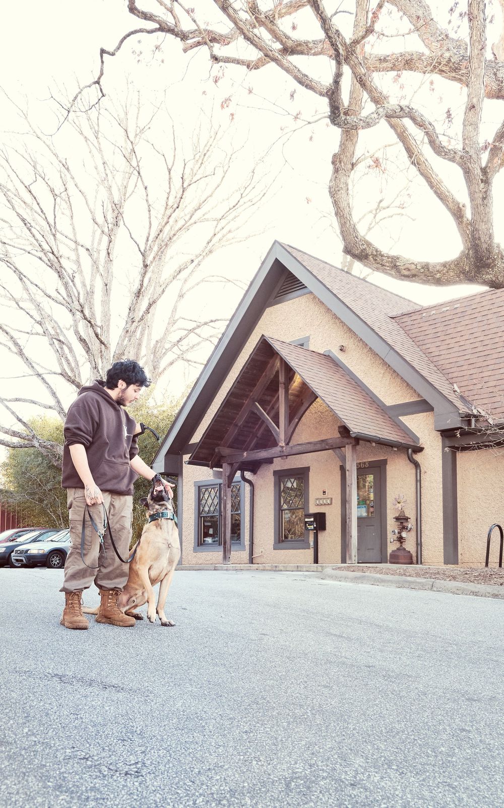 Someone stands with their dog in front of a rustic building entrance with timber frame details and bare winter trees.