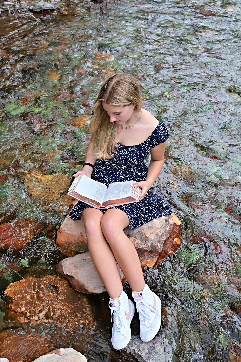 senior portrait of a girl sitting on a rock in the middle of a crystal clear stream reading a bible glacier national park montana