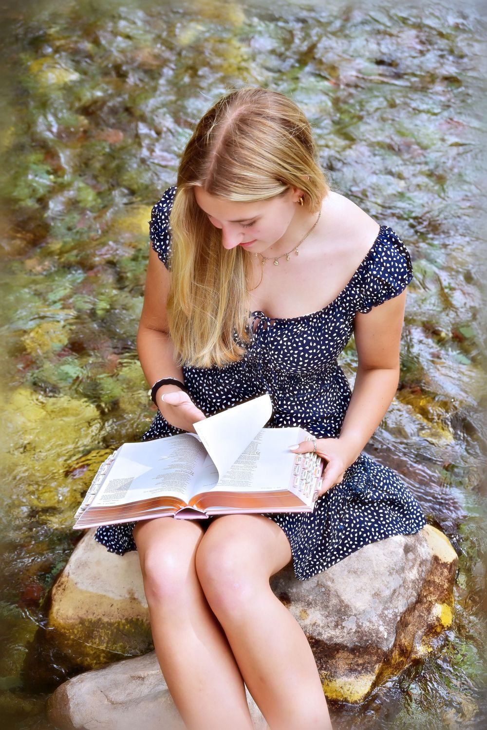 senior portrait of a girl sitting on a rock in the middle of a crystal clear stream reading a bible glacier national park montana