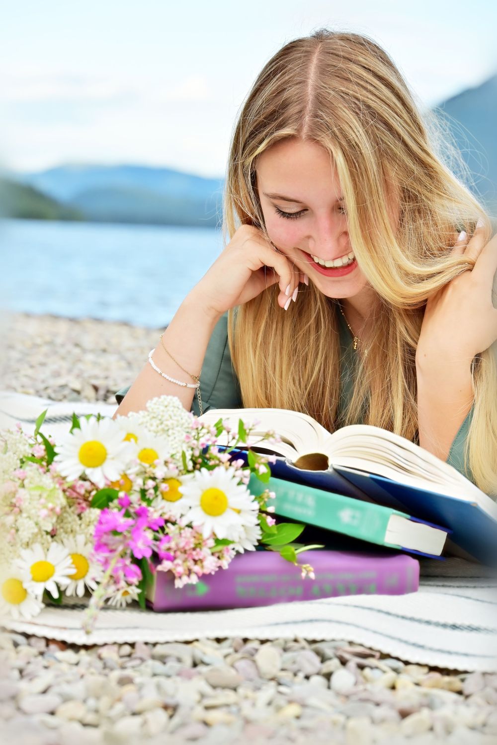 senior portrait of a girl reading books with wildflowers laughing on the shore of lake McDonald glacier national park