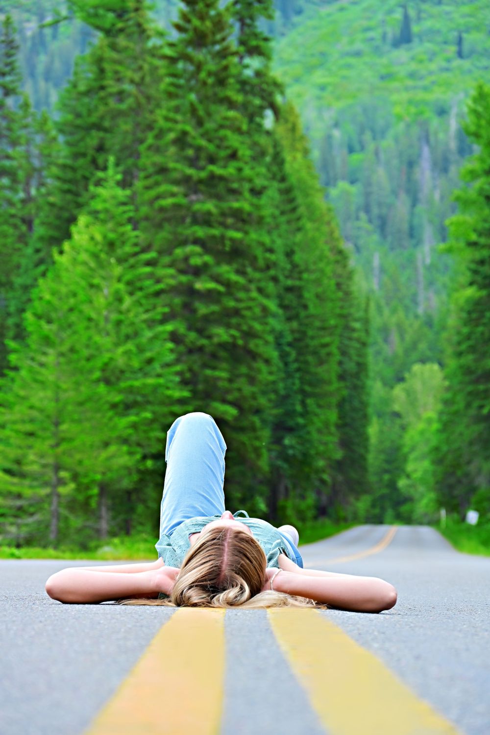 senior portrait of a girl laying in the middle of the road on the yellow line glacier national park montana