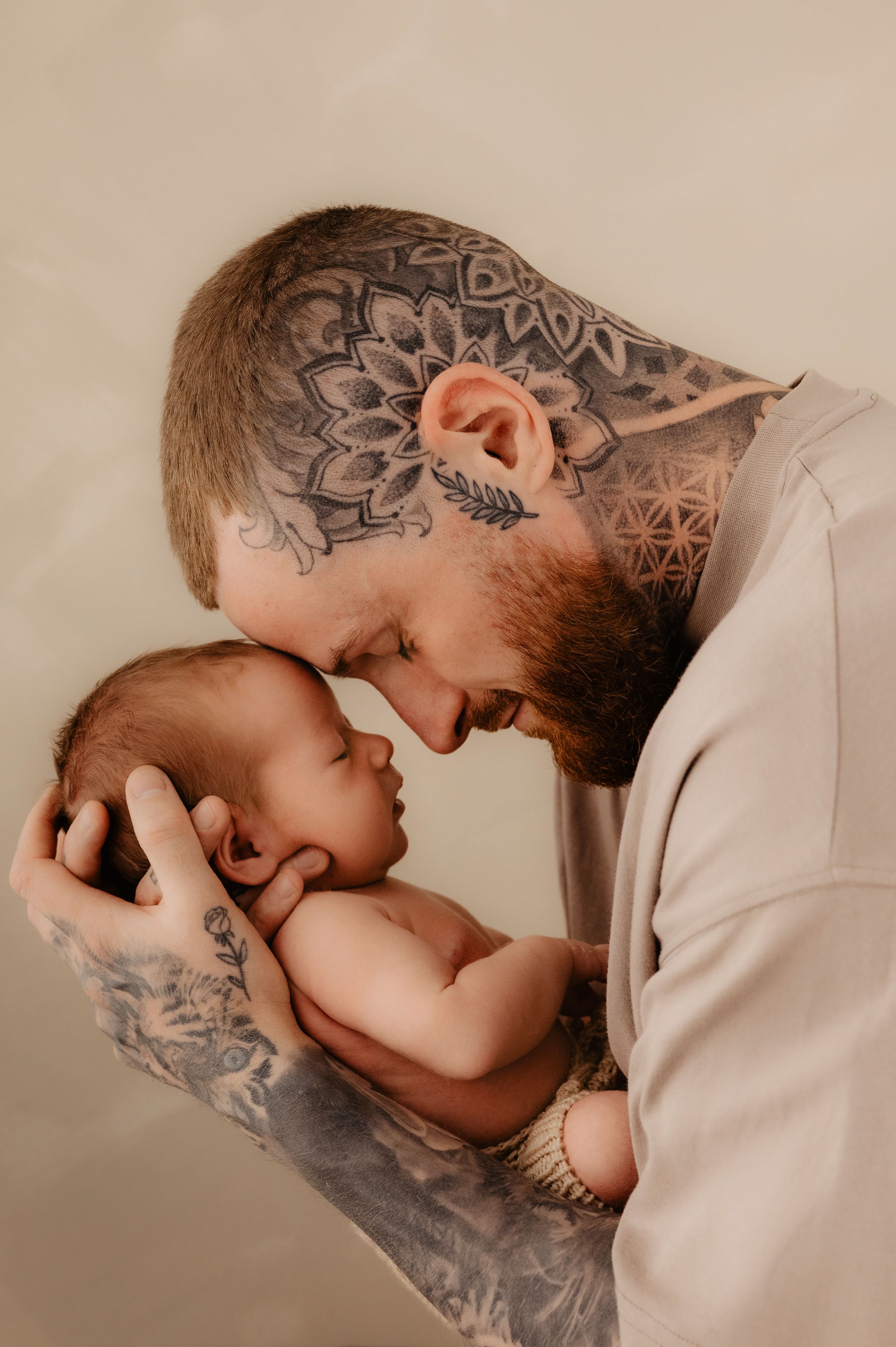 Intimate newborn photography with parent and baby showing tattooed arms in neutral tones.